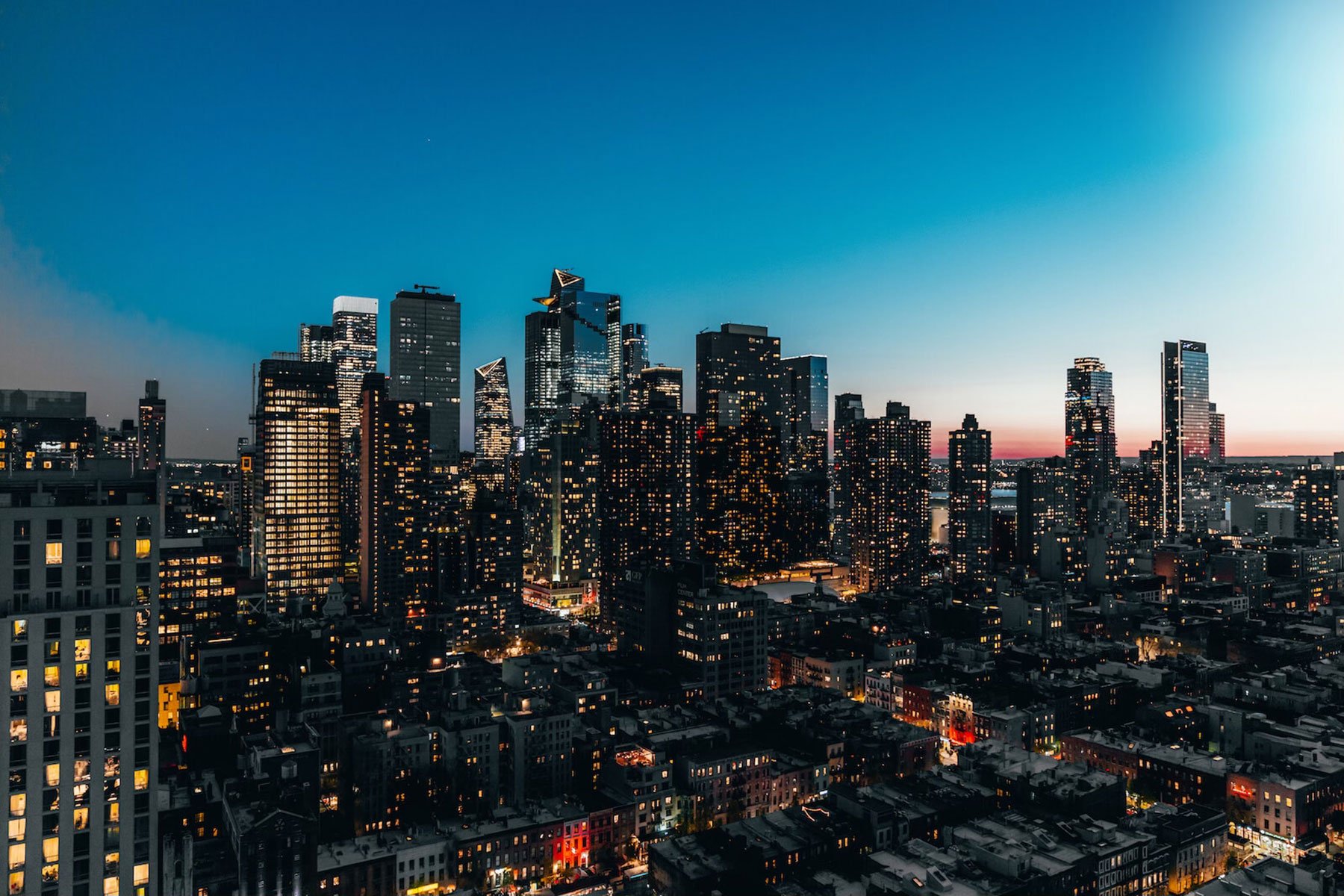 Starchild Rooftop at dusk, with skyline views over a city of tall lit towers and low rooftops under a deep blue sky