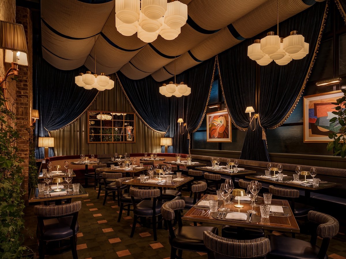 Carversteak dining room with navy velvet drapery, glowing globe chandeliers, and set tables with wine glasses and brass lamps